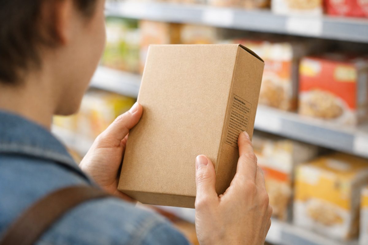 Shopper in a supermarket aisle reading the ingredient panel on a cereal box